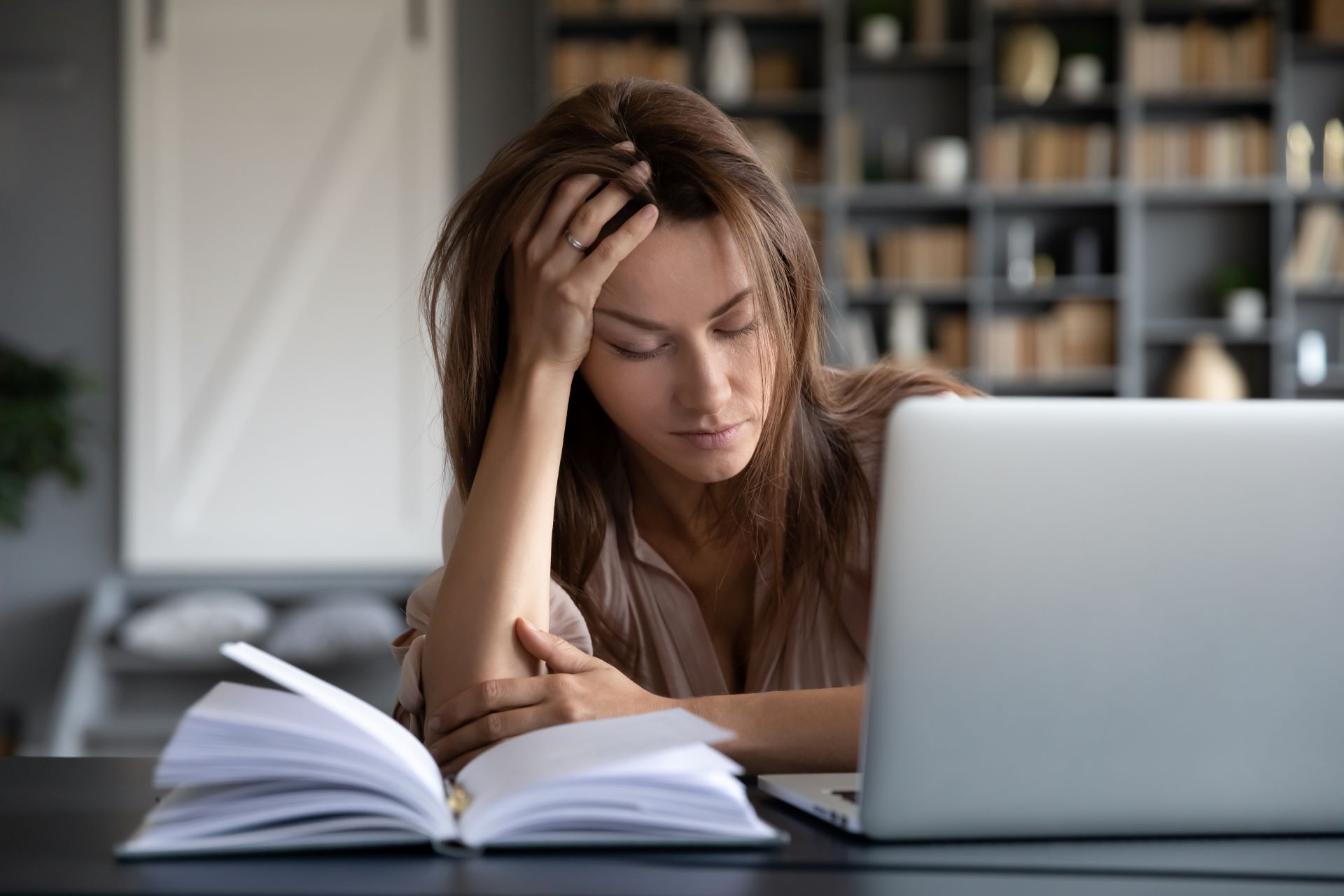 Erschoepfte Frau mit Kopf in der Hand vor Laptop